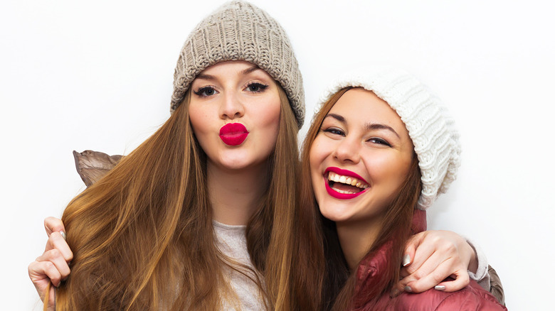 Two women in winter clothes and hats wearing bright lipstick