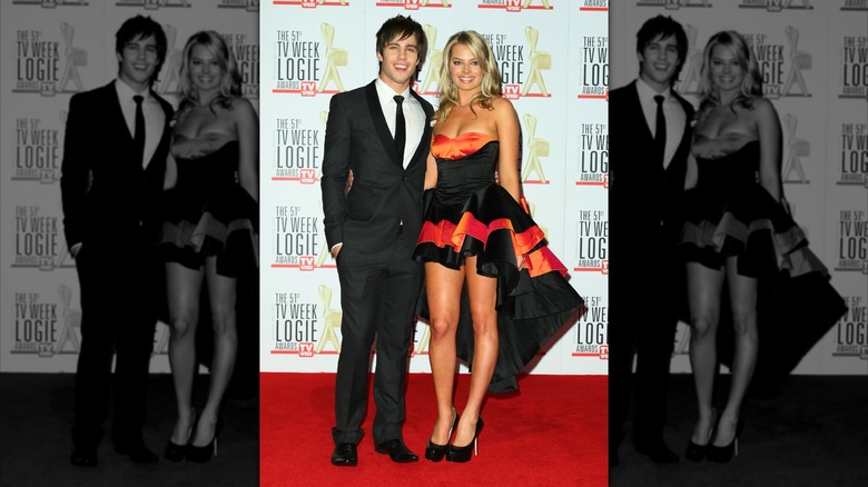 Dean Guyer and Margot Robbie posing at the Logie Awards in 2009. Guyer is in a black suit and Robbie is in an orange and black high-low dress.
