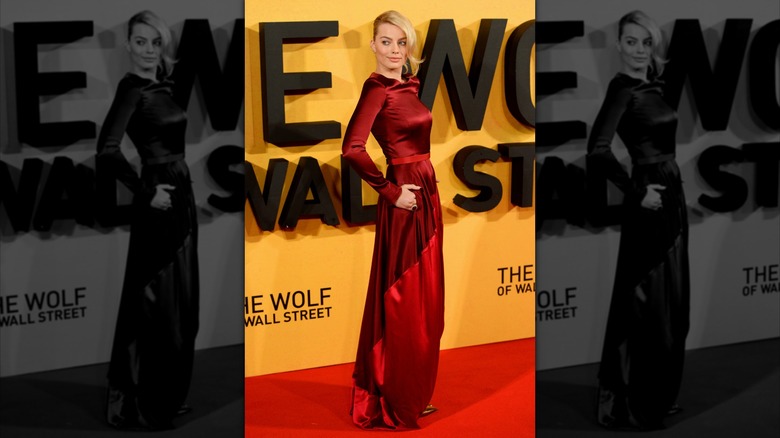 Margot Robbie at the UK premiere of "The Wolf of Wall Street" wearing a red gown with her hair swept to one side and looking away from the camera