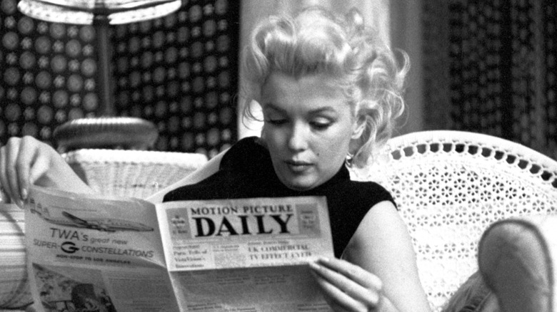 A black and white photo of Marilyn Monroe reading a newspaper.