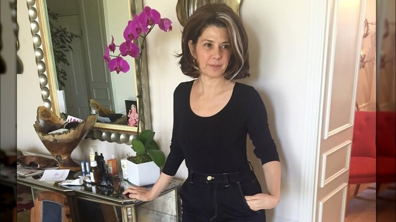Marisa Tomei wearing an all-black outfit and a bouffant wig with a gray streak
