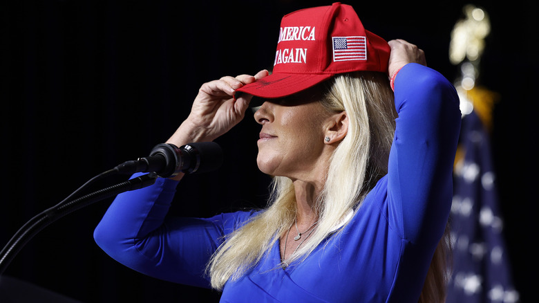 Marjorie Taylor Greene proudly putting on a MAGA hat in front of a microphone
