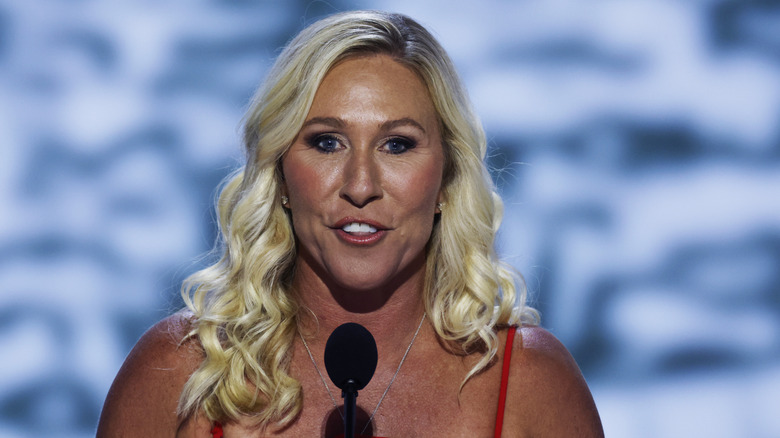 Marjorie Taylor Greene smiling in a red dress at the Republican National Convention with a microphone in front of her face.