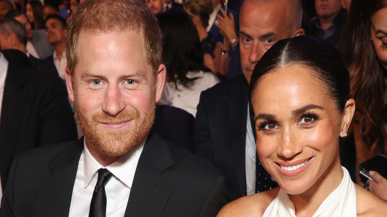 Meghan Markle and Prince Harry smiling while sitting an event together