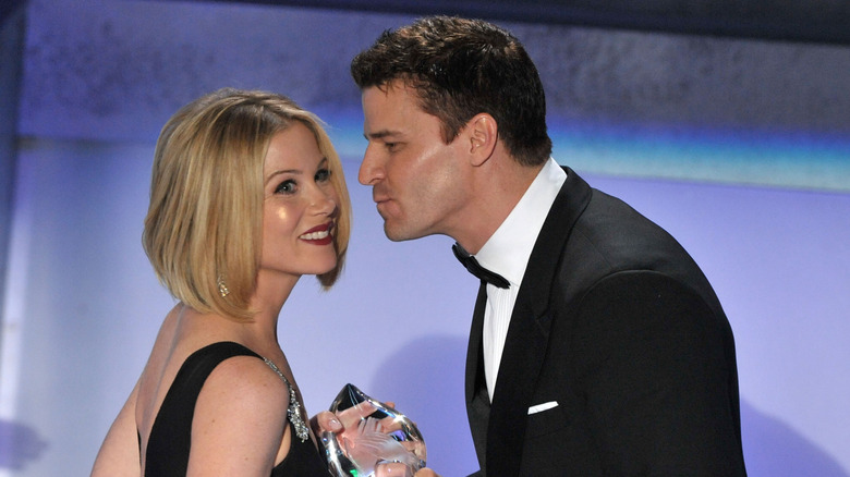 David Boreanaz in a suit leaning in to kiss Chirstina Applegate's cheek as she holds an award.