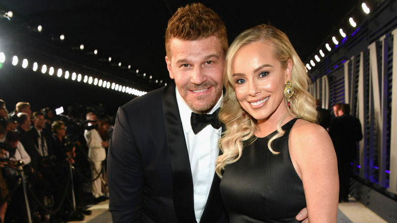 David Boreanaz in a tuxedo smiling while embracing Jaime Bergman in a black dress.