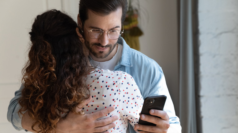 Man hugs wife while texting another woman