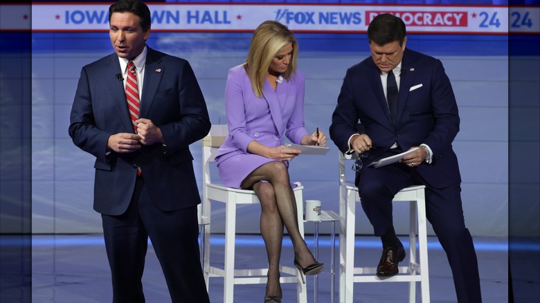 Martha MacCallum wearing a light purple dress and tights while with Brett Baier and Ron DeSantis who are wearing suits.