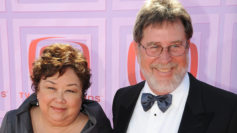 Kellye Nakahara and David Wallett smiling on step-and-repeat