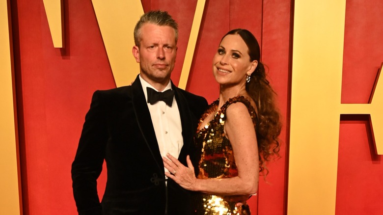 Addison O'Dea wearing a tuxedo posing next to Minnie Driver in a gold dress.