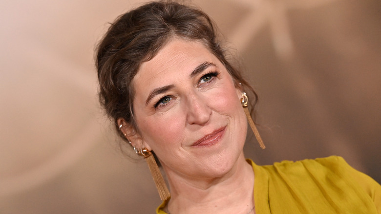 Mayim Bialik smiles in a mustard yellow shirt