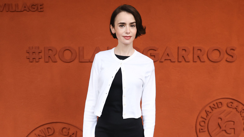Lily Collins posing in a black dress with a white cardigan in 2026.