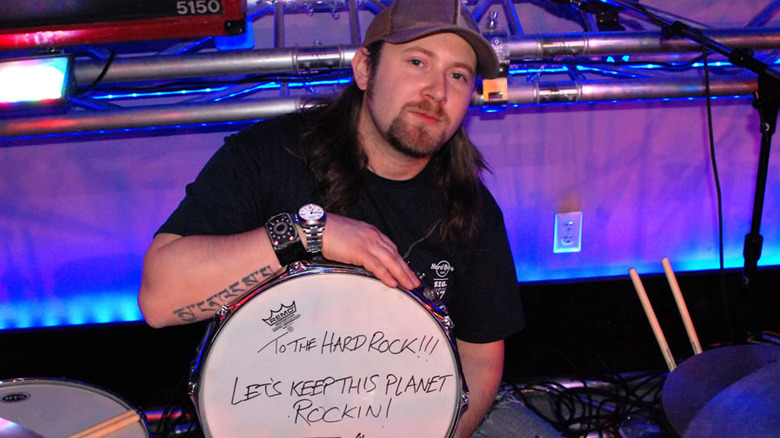 Simon Collins posing with a drum that reads "To the Hard Rock, let's keep this planet rocking."