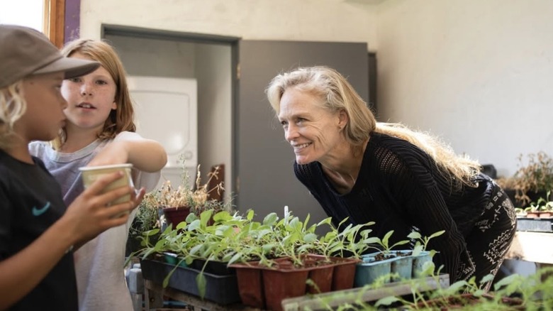 Suzy Amis smiling over a bed of plants at a couple of kids