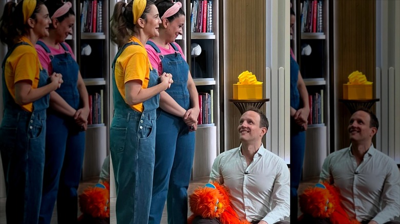 Drew Barrymore and Ms. Rachel in matching overalls, with Aron Accurso sitting on the ground looking up at his wife lovingly