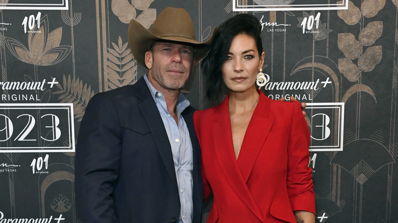 Taylor Sheridan posing in a cowboy hat and a suit with his wife Nicole Muirbrook in a red dress