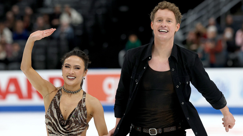Madison Chock wears a zebra pattern sparkle dress while holding hands with Evan Bates on the ice smiling at the crowd