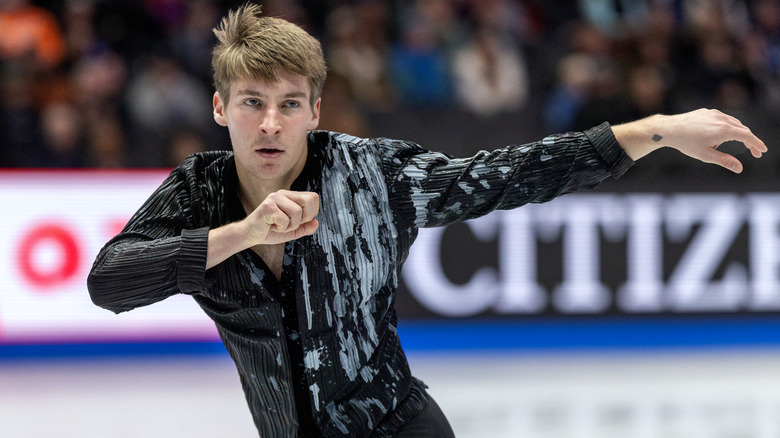 Andrew Torgashev skates in a black and white shirt with his arms out to the left