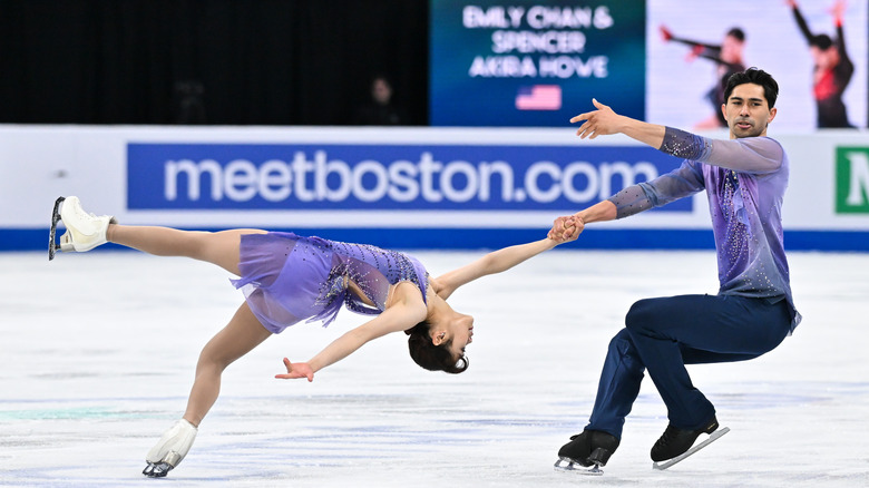 Emily Chan and Spencer Akira Howe wear matching purple outfits as Howe holds her hand while she is horizontal ice skating