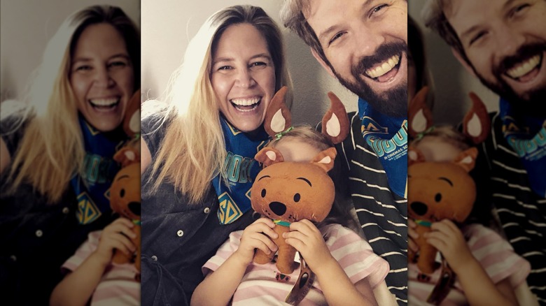 Mary Grill and Matt Hobby posing with their kid whose face is obscured by a Scooby Doo toy
