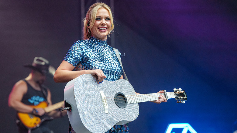 Megan Moroney smiling while performing onstage with a guitar