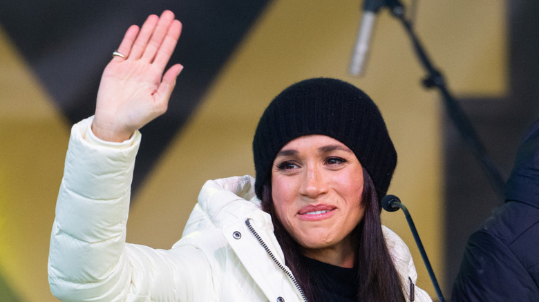 Meghan Markle waving in a beanie hat and white puffer jacket