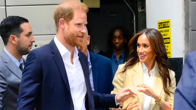 Prince Harry in a blue blazer and Meghan Markle in a yellow jacket exiting the stage door.