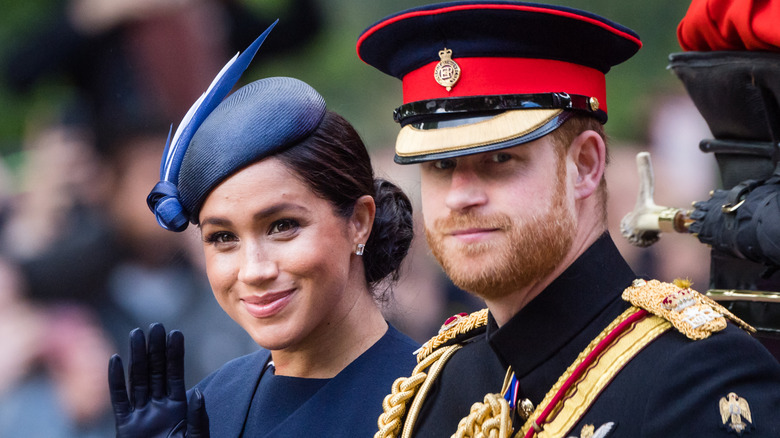 Meghan Markle waving at the crowd while Prince Harry looks on