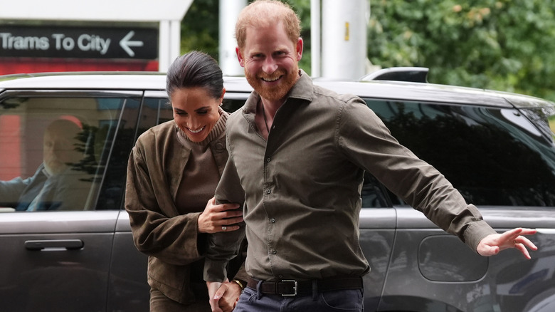 A smiling Meghan Markle holding onto a laughing Prince Harry's arm in matching olive green outfits