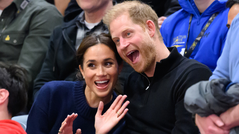 Meghan Markle and Prince Harry smiling while sitting in a crowd