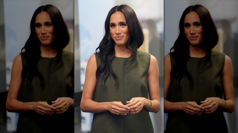 Meghan Markle smiling in a dark green dress.