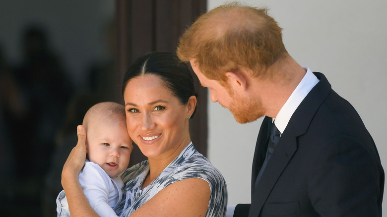 Meghan Markle holding Archie with Harry looking on