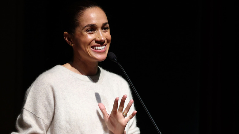Meghan Markle delivering a speech onstage in a cream sweater