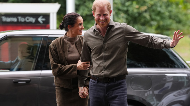 Meghan Markle holds Prince Harry's arm as they smile and wave at onlookers