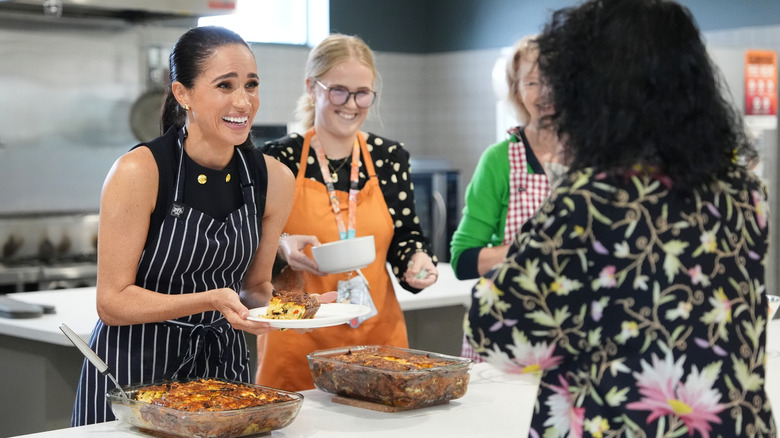Meghan Markle handing someone a plate of food in an apron