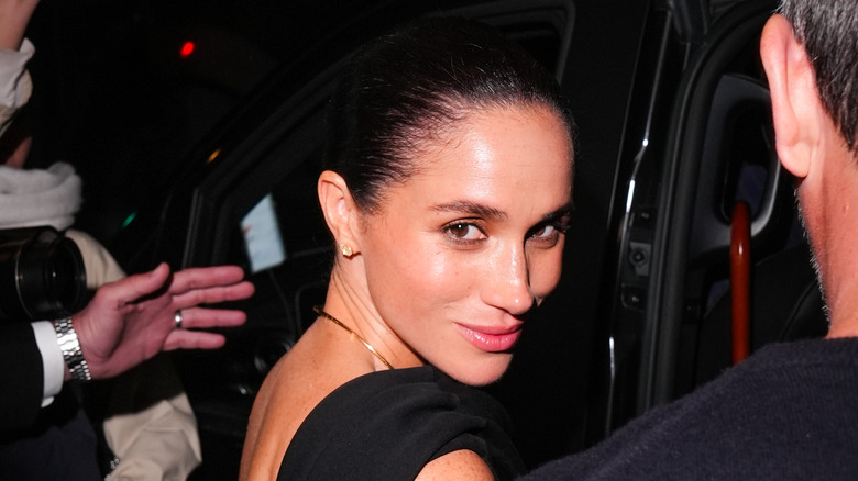 Meghan Markle smiling while looking over her shoulder as she gets into a car