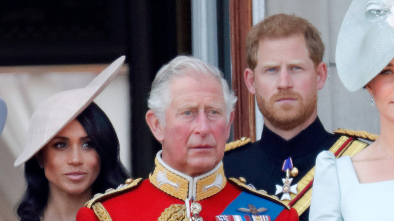 Meghan Markle and Prince Harry stand behind King Charles III