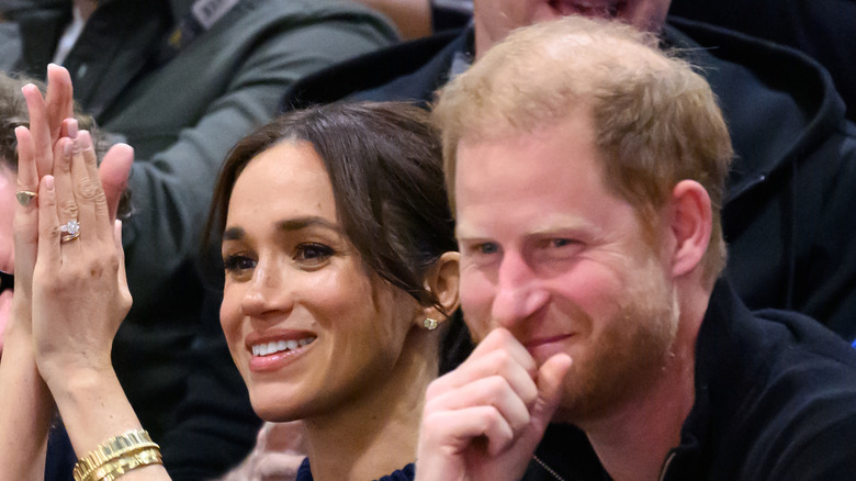 Meghan Markle claps while sitting next to Prince Harry
