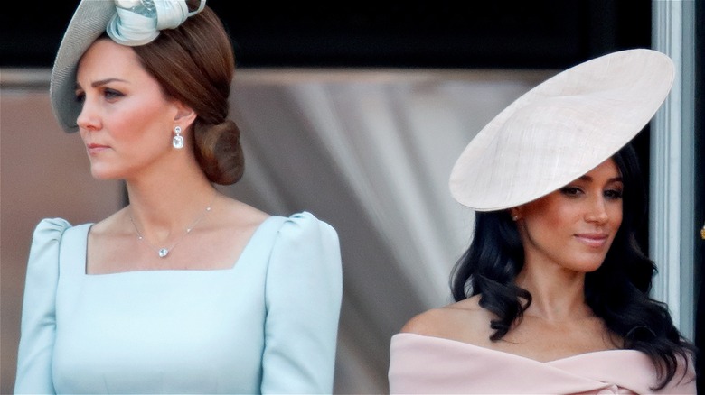 Kate Middleton and Meghan Markle standing side by side, looking in opposite directions