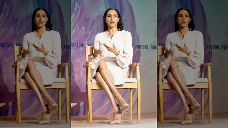 Meghan Markle in a wooden chair with a microphone by her mouth.