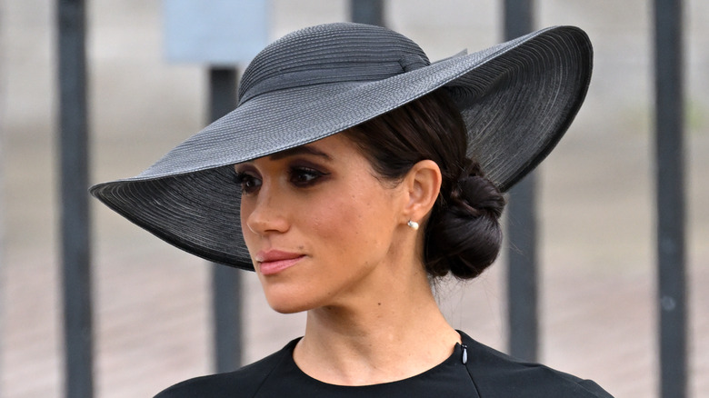 Meghan Markle in a black hat with her hair tied back in a bun.