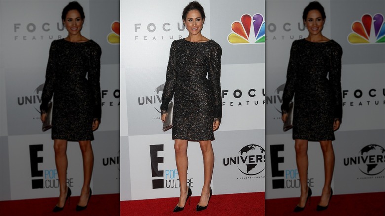 Meghan Markle smiles in front of NBC logo on red carpet.