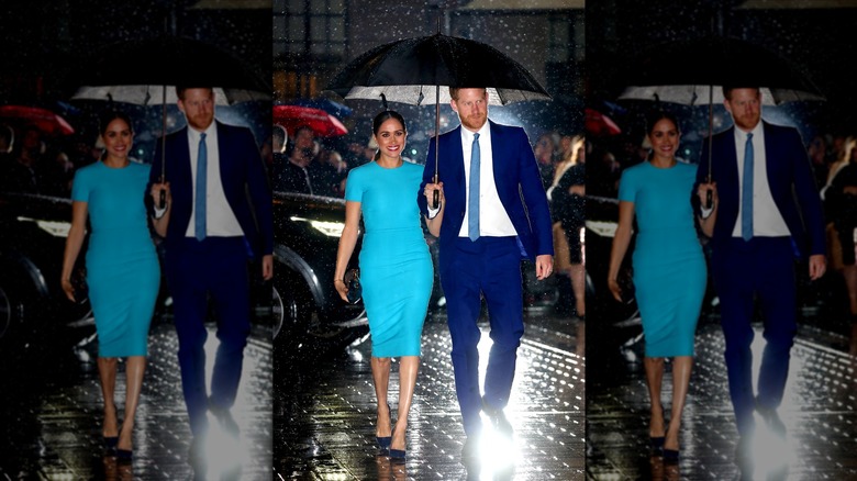 Prince Harry and Meghan Markle wearing blue while walking under an umbrella in the rain