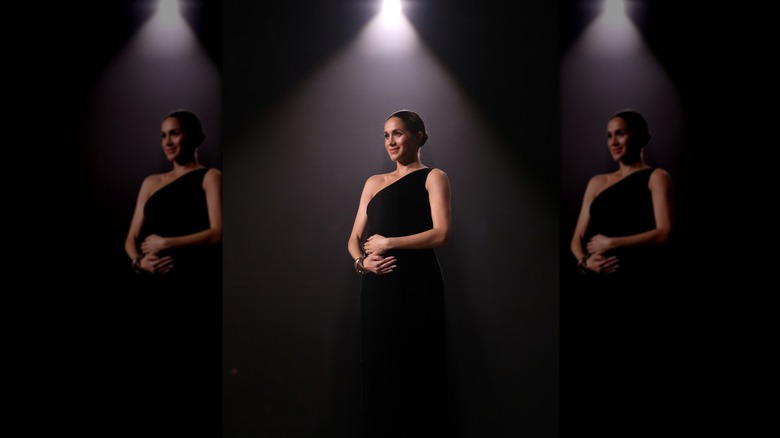 Meghan Markle standing under a spotlight in a black dress