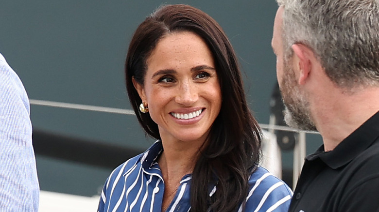 Meghan Markle wearing a blue and white stripes shirt and smiling at a man with gray hair.