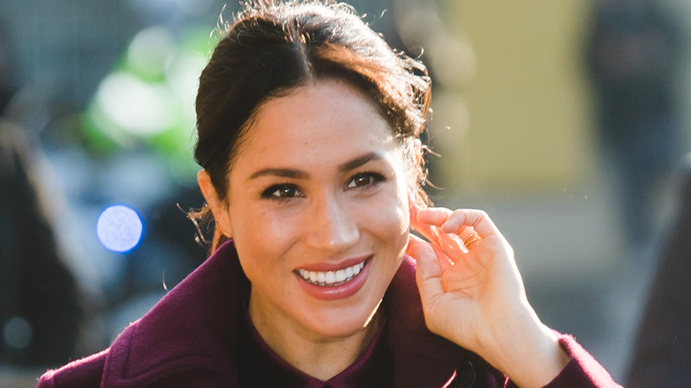 Meghan Markle smiling and touching her ear