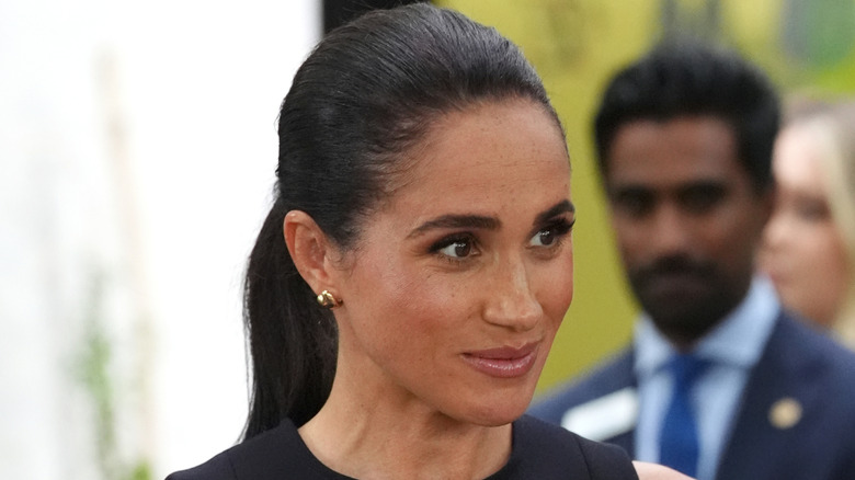 Meghan Markle wears her hair in a ponytail and smiles while looking to the left.