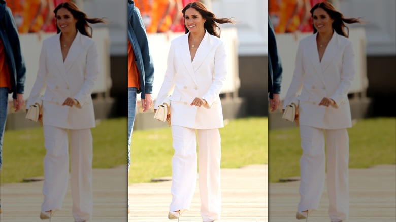 Meghan Markle walking and smiling in white pantsuit