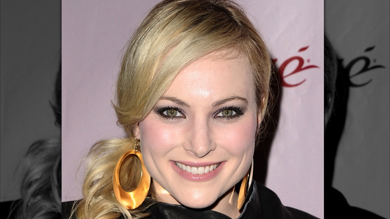 Meghan McCain smiles while wearing large hoop earrings and heavy face powder.