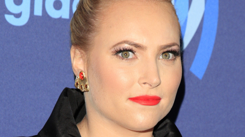 Meghan McCain poses in front of a blue background wearing black.